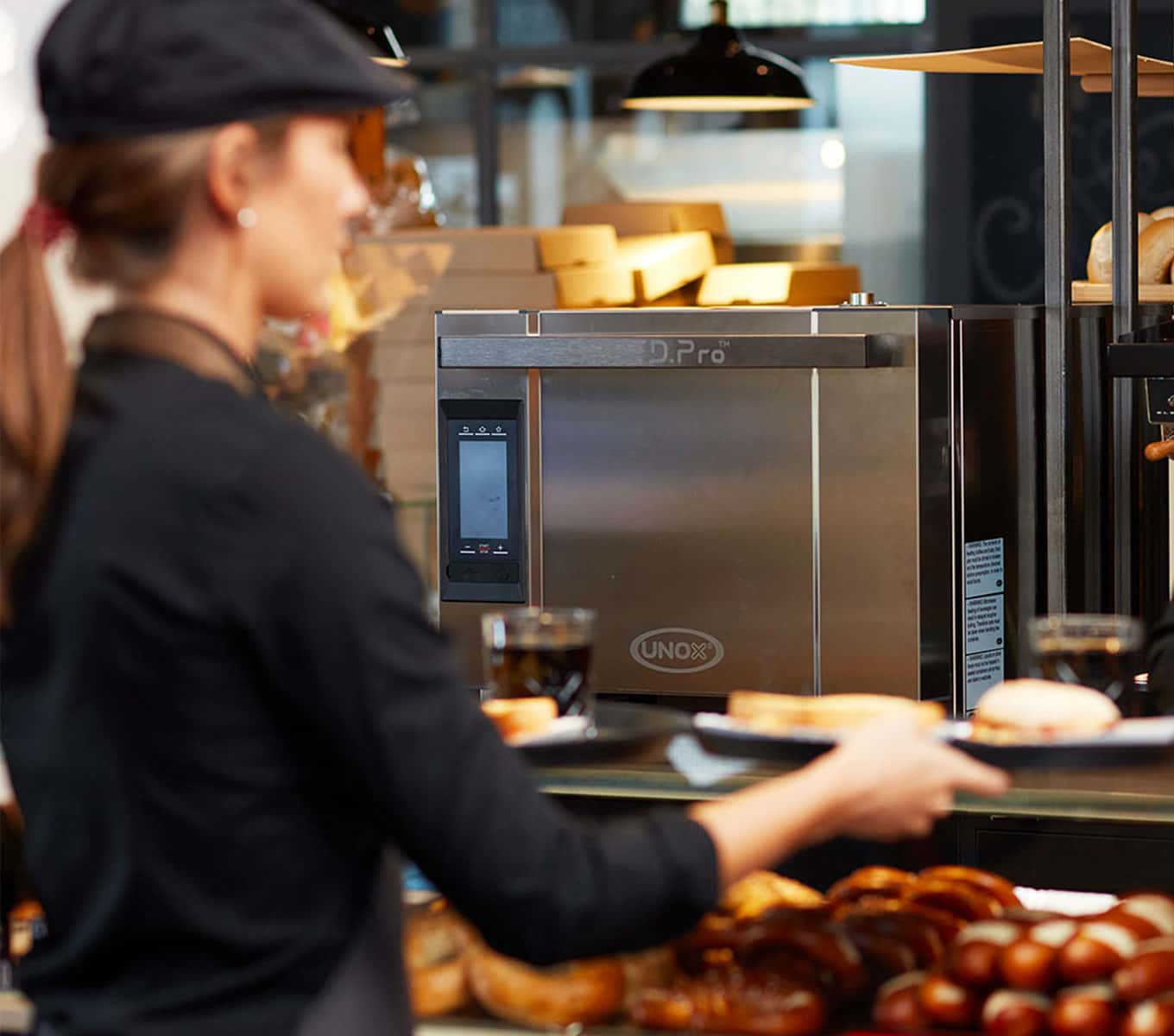 En barista tager en bakke fra disken med en Unox SPEED.Pro professionel hastighedsovn i baggrunden