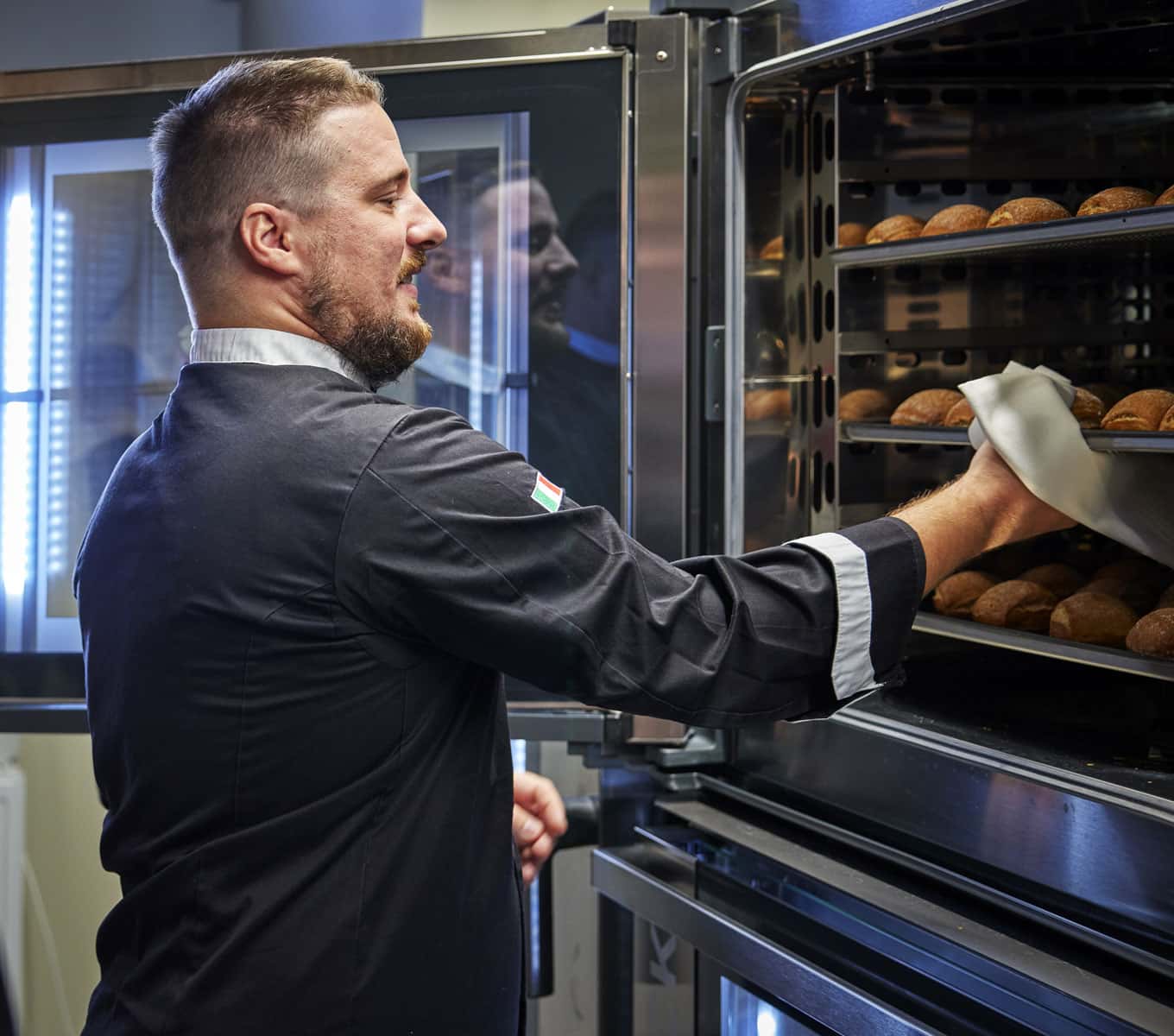 Mandlig kok tager en bakke croissanter ud af en Unox kombiovn til professionel konditori