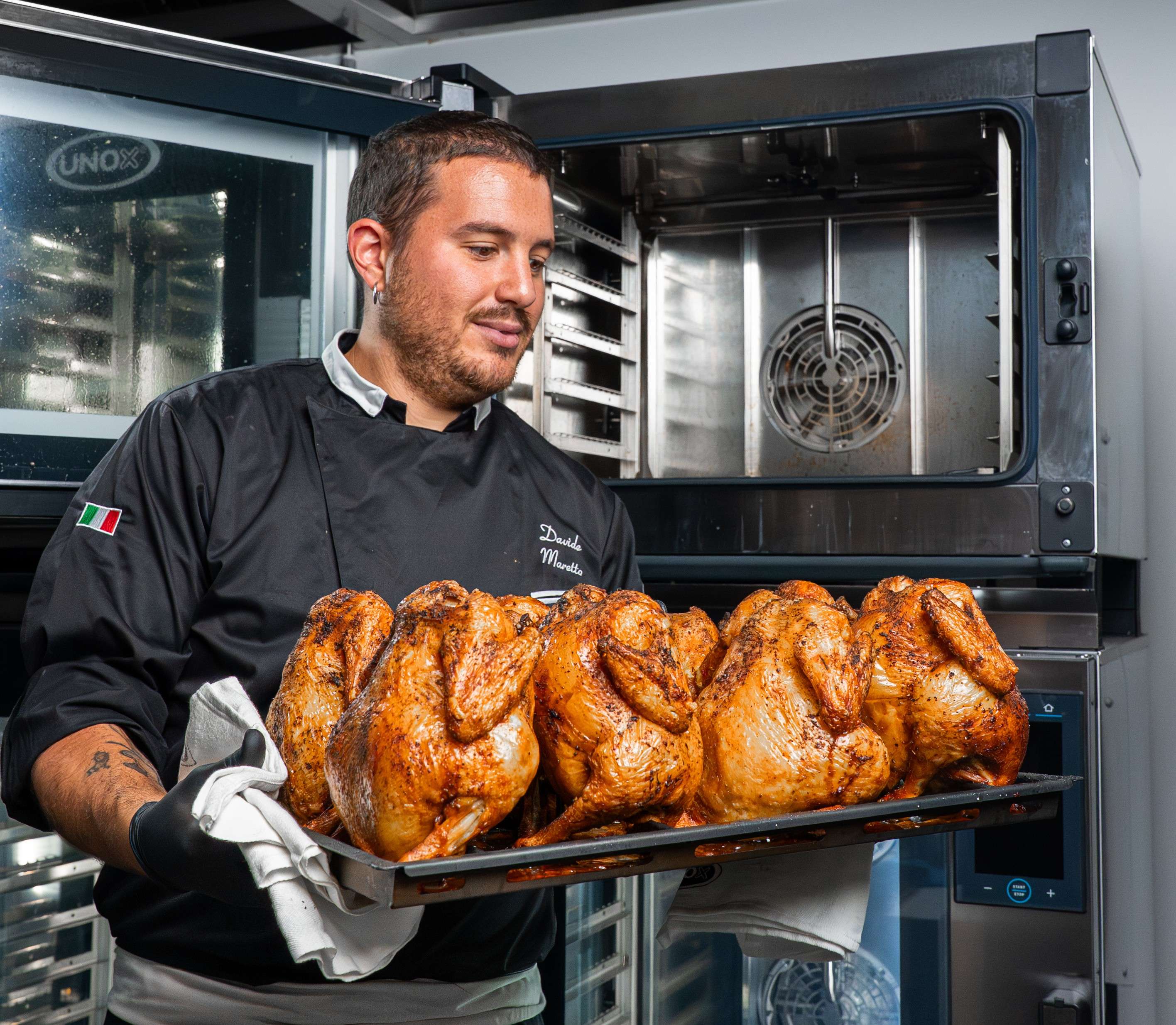 chef hombre mira una bandeja de pollos asados recién sacada del horno mixto profesional Unox detrás de él