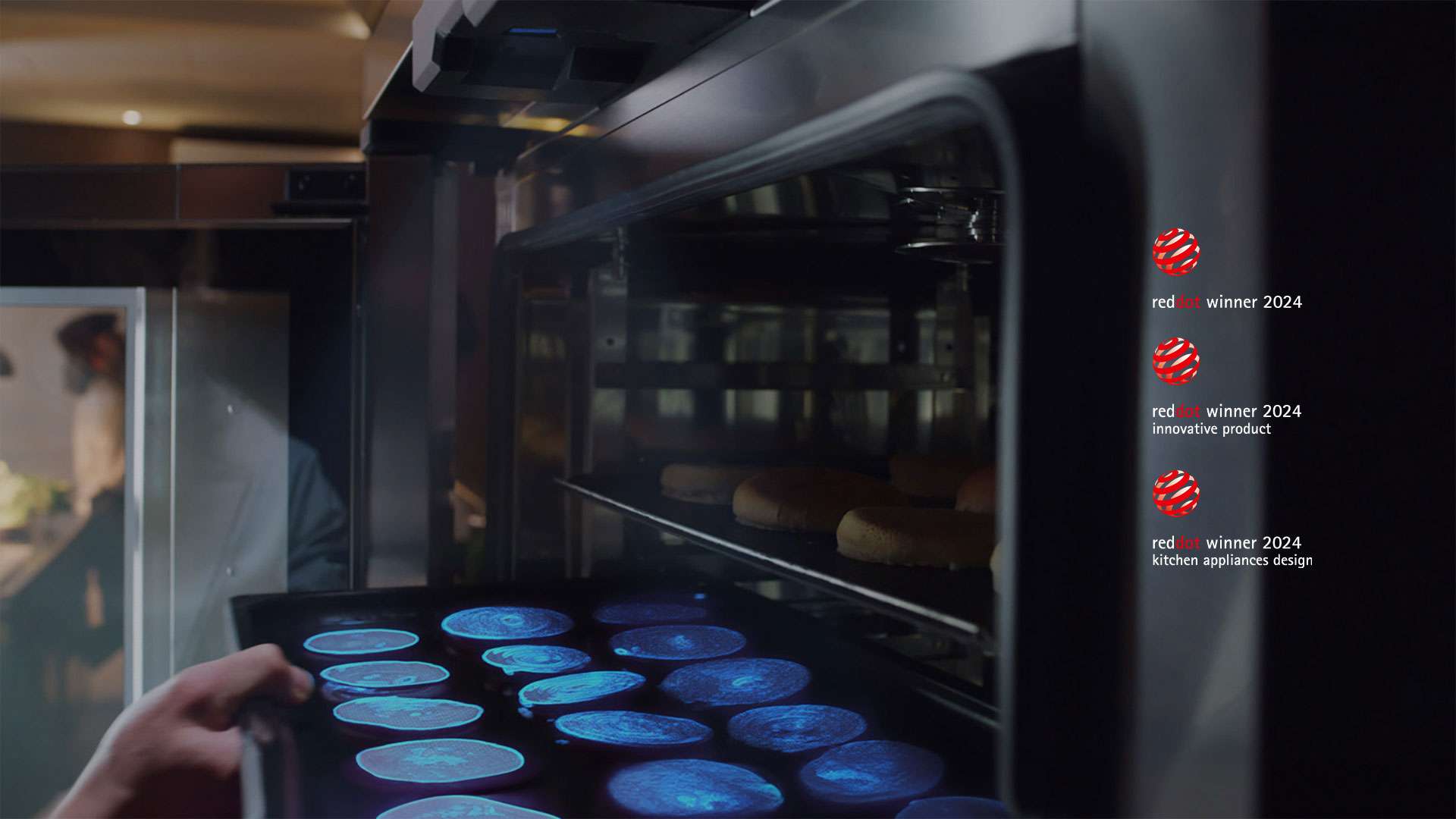 A hand puts a tray of food into an oven. A sensor at the top shines a blue light on the food to scan and identify what the food is.