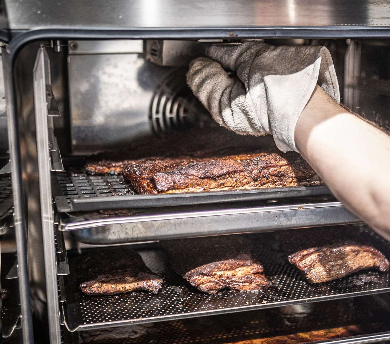 Eine geöffnete Garraum eines Unox Kombidämpfers mit Schweinerippchen darin und einem installierten Räucherzubehör