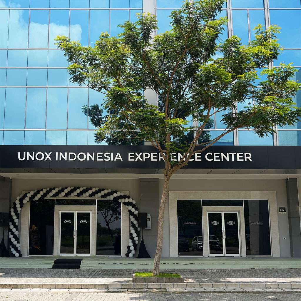 Facade of the UNOX Indonesia Experience Center featuring glass doors, a black sign with white lettering, and a decorative arch of black and white balloons.